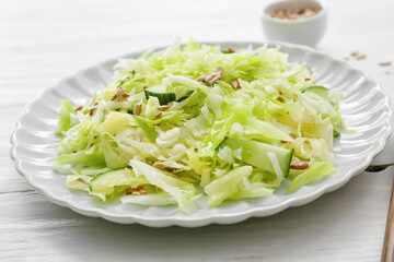 Plate with tasty cabbage salad on light wooden table, closeup