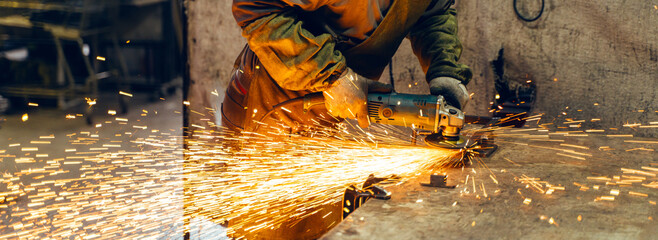 Locksmith in special clothes and goggles works in production. Metal processing with angle grinder....