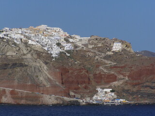looking up at the town of  oia, santorini, greece, on a sunny day from a boat in the aegean sea