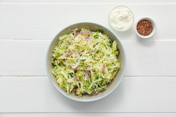 Bowl with tasty cabbage salad, sauce and flax seeds on light wooden table