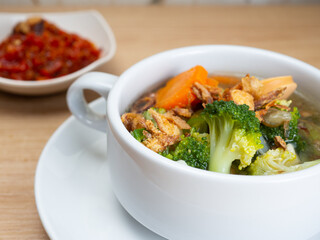 Vegetables soup that contain sausage, broccoli, carrots, etc on a white porcelain bowl