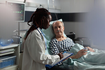 African american doctor in hospital room discussing diagnosis and treatment with sick senior man...