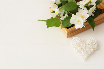 Box with beautiful jasmine flowers on light wooden background