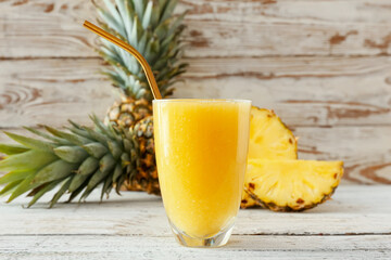 Glass of tasty pineapple smoothie on light wooden background