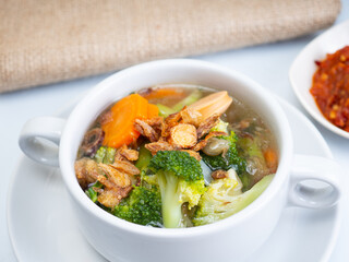 Vegetables soup that contain sausage, broccoli, carrots, etc on a white porcelain bowl