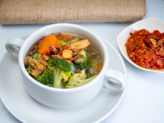 Vegetables soup that contain sausage, broccoli, carrots, etc on a white porcelain bowl