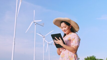 Asian young woman using a digital tablet in the field in the background wind power production turbines.
