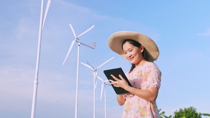 Fototapeta premium Asian young woman using a digital tablet in the field in the background wind power production turbines.