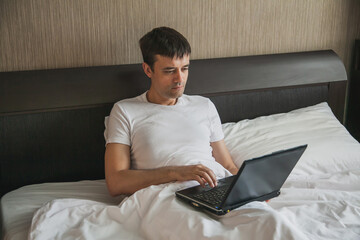 A middle-aged man is sitting in bed in his bedroom and working on a laptop