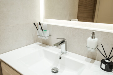 Bright bathroom interior with white sink and toothbrushes, flavoring and liquid soap on it - 444213153