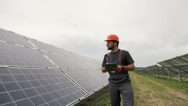 Male engineer with digital tablet PC walking near modern photovoltaic solar panels. Clean energy production. Solar farm.