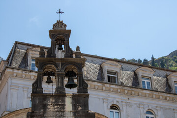 Medieval church with three ancient bells on the background of the facade with the windows of the old building and the blue sky.