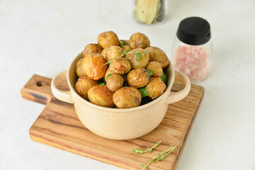 Pot with tasty baked potato on light background
