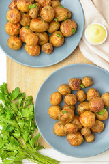 Plates with tasty baked potato and sauce on light wooden background
