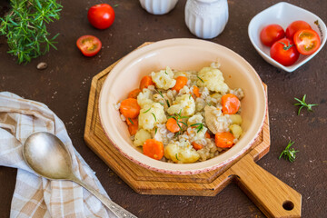 Hearty stew with chicken, barley, carrots and cauliflower in a ceramic bowl on a brown concrete background.