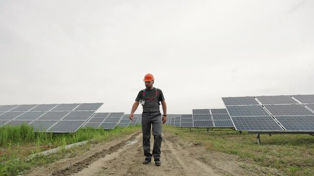 Professional male engineer in protective helmet walks on ecological solar plant construction. Concept of electricity, ecology, technologies. Farm of solar panels.