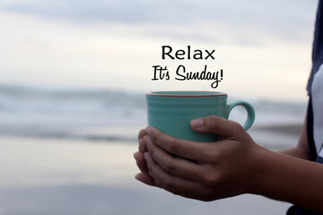 Relax. It's Sunday. Hello Sunday weekend concept with a person holding a cup of coffee in hand on beach background. Happy Sunday. Self love care and happiness concept. - obrazy, fototapety, plakaty
