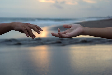 Helping hands of two people reaching out each other on beach background. Hope, kindness and...