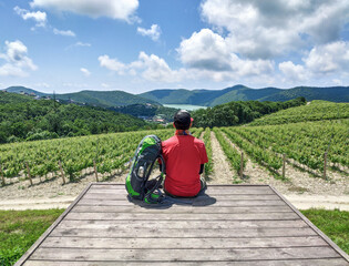 Man with backpack sitting on wooden platform at vineyard and mountains background. Panoramic...