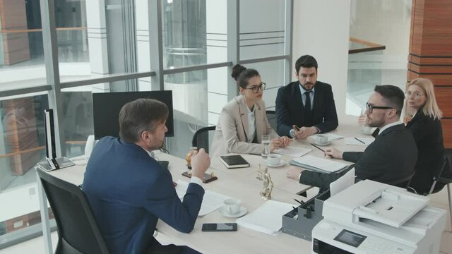 High-angle slowmo shot of team of professional lawyers or attorneys and their director conferencing at meeting table about case