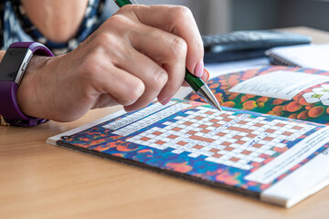 a womans hand with a pen writes solutions to a crossword puzzle