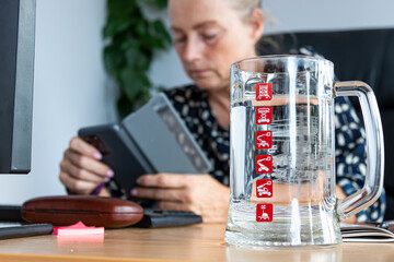 middle-aged woman working in the office, on the table in the foreground a glass cup with water