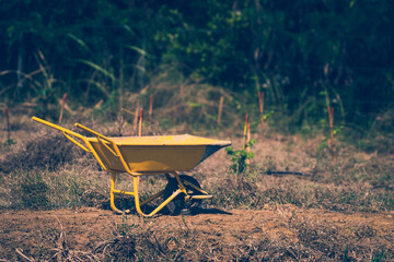 Yellow Construction cart  In the garden in the dry sun.Arid land and dead grass