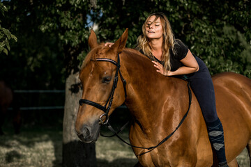 Obraz premium Beautiful young woman riding beautiful well-groomed horse on summer evening. Concept of beauty and health. Active recreation. Equestrian sports. Enjoying life.