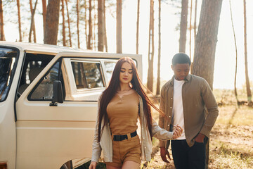 Near the white bus. Young couple is traveling in the forest at daytime together