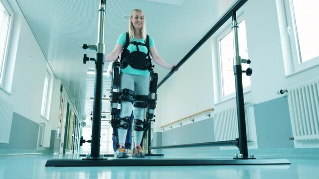 A lady is learning to walk in the exosuit with medical help