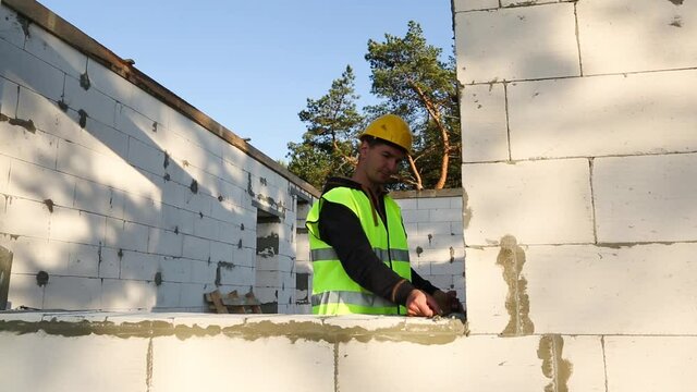 Construction worker at construction site measures the length of the window opening and the wall with tape measure. Cottage are made of aerated concrete blocks, protective clothing - hardhat and a vest