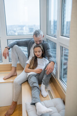 A dad sitting at the window with his daughter