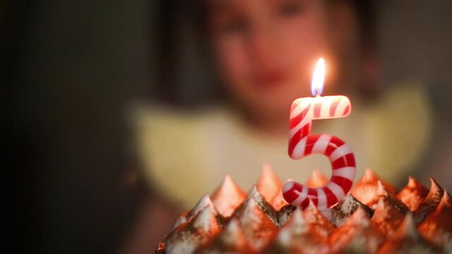 The girl looks at the burning candle with the number 5 on the cake and makes a wish. Birthday, fifth anniversary, five years, candle flame, orange fire. Children's holiday. Close-up