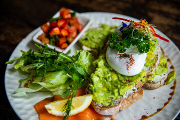 Healthy avocado toast on gluten free bread with poached eggs and green salads with tomatos on white plate in cafe.