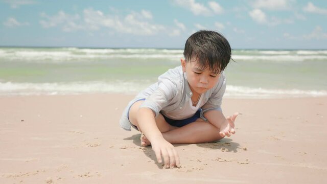 asian boy child scribble in the sand at the beach on the summer day.