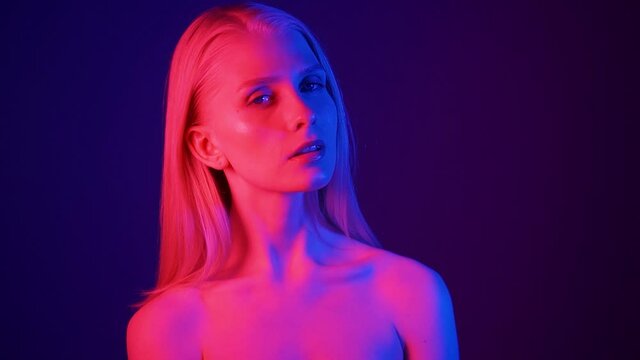 Portrait of a young attractive woman in colored lighting. Red, blue and purple lights illuminate the model's face. Close-up, slow motion, HD.