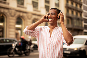 Cheerful guy listening the music with the headphones. Young african man using the phone outdoors.