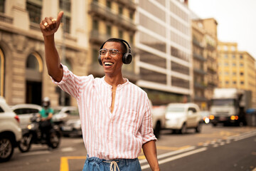 Cheerful guy listening the music with the headphones. Young african man using the phone outdoors.