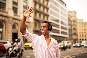 Cheerful guy listening the music with the headphones. Young african man using the phone outdoors.