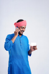 Young indian man in traditional wear and talking on smartphone and using card over white background.