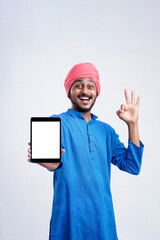 Young indian man in traditional wear and showing tablet over white background.