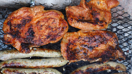 marinated chicken meat and sausages are cooked in nature on a metal barbecue net . top view . outdoor recreation