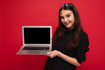 Photo of beautiful smiling brunet girl wearing black clothes holding computer laptop looking at camera isolated on colourful wall background
