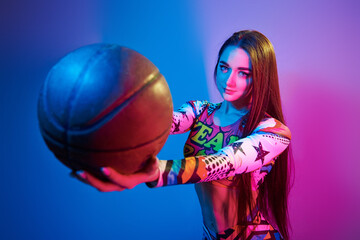 In colorful clothes. Fashionable young woman standing in the studio with neon light