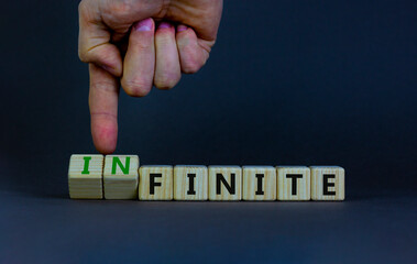 Finite or infinite symbol. Businessman turns wooden cubes and changes the word 'finite' to 'infinite'. Beautiful grey table, grey background. Business, finite or infinite concept. Copy space.