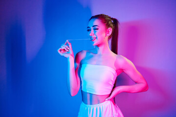 With chewing gum. Fashionable young woman standing in the studio with neon light