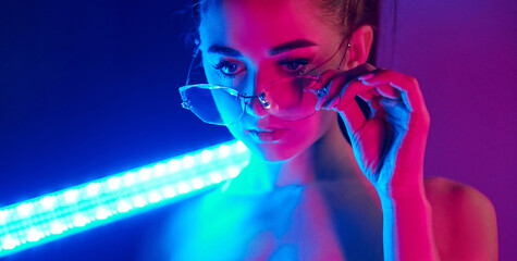 Holds neon lighting stick. Fashionable young woman standing in the studio