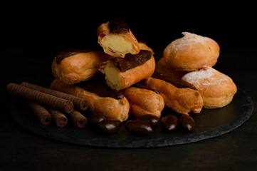 Blurred image of eclairs, assorted desserts and chocolate covered almonds on a slate tray against a dark background.