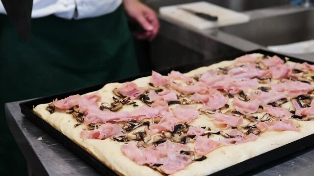 pizza to take away cooking. The process of making a rectangular Roman pizza in pieces "Pizza al taglio" in a pizzeria. the chef puts mozzarella cheese and ham  on the dough