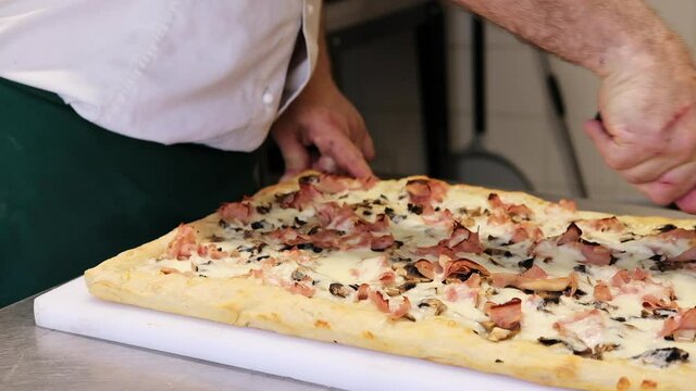 pizza to take away cooking. The process of making a rectangular Roman pizza in pieces "Pizza al taglio" in a pizzeria. the chef puts mozzarella cheese and ham  on the dough